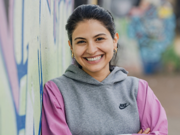 ESMT Berlin Full-time MBA alum Farah Nafi' standing by a graffitied wall in central Berlin and smiling