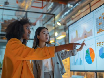 Two female students pointing at a screen with financial graphs and charts