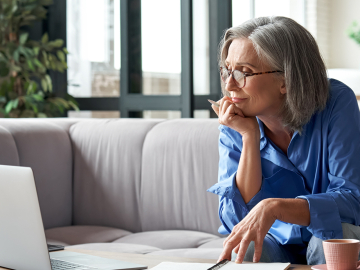 Woman sitting on couch working on laptop placed on coffee table. 