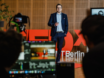 Stefan Wagner speaking at TEDx event at ESMT with blurred view of camera and camera man in front of the stage 