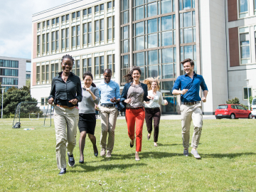 Six students running towards the camra on a green field. 
