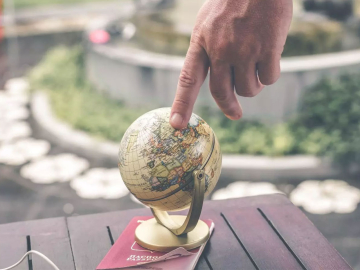 A person's hand touching a small globe atop a passport