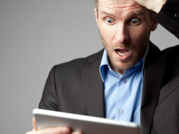 Whie male in a business suit with a shocked expression on face looking at tablet. 