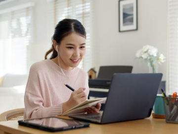 Asian female attending a webinar, writing in her notepad