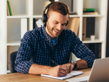 man with headphones writing on a notepad
