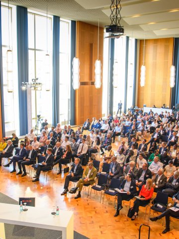 Speaker delivering a keynote presentation to a large audience in a modern auditorium at ESMT Berlin