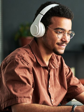 Man in his early twenties watching a webinar on his computer. He is wearing large white headphones