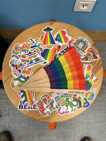 A rainbow fan with ESMT Berlin written on the handle, surrounded by rainbow-themed stickers