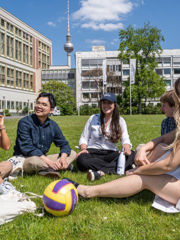 ESMT Berlin students sitting together on the campus lawn with the Berlin TV Tower in the background.