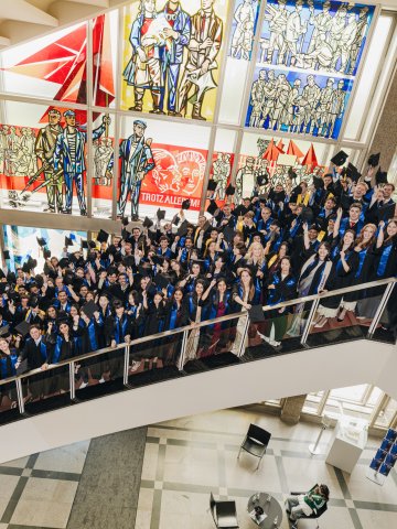 Students from the ESMT Berlin master's class standing on the campus staircase in their caps and gowns and smiling