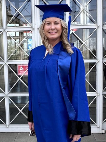 ESMT Berlin Executive MBA graduate Mary Oxley in her mortarboard and gown, standing in front of the school on graduation day.