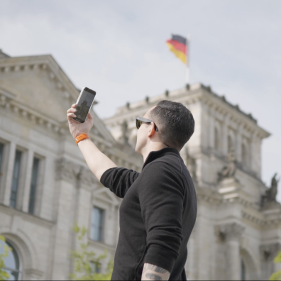 An ESMT Berlin Full-time MBA student taking a picture of the Bundestag in Berlin on his phone. The German flag is visible at the top of the building