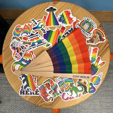 A rainbow fan with ESMT Berlin written on the handle, surrounded by rainbow-themed stickers