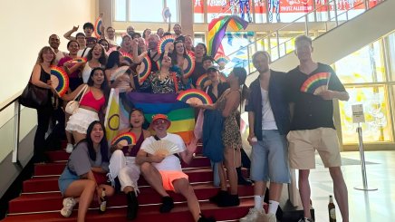 Students from the ESMT Pride Impact club posing for a group photo on campus. They have rainbow flags and fans.