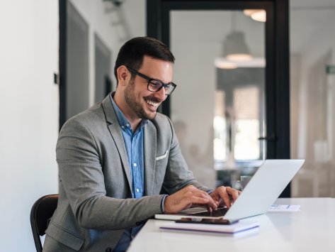 Cheerful male professional working on laptop while sitting at office desk