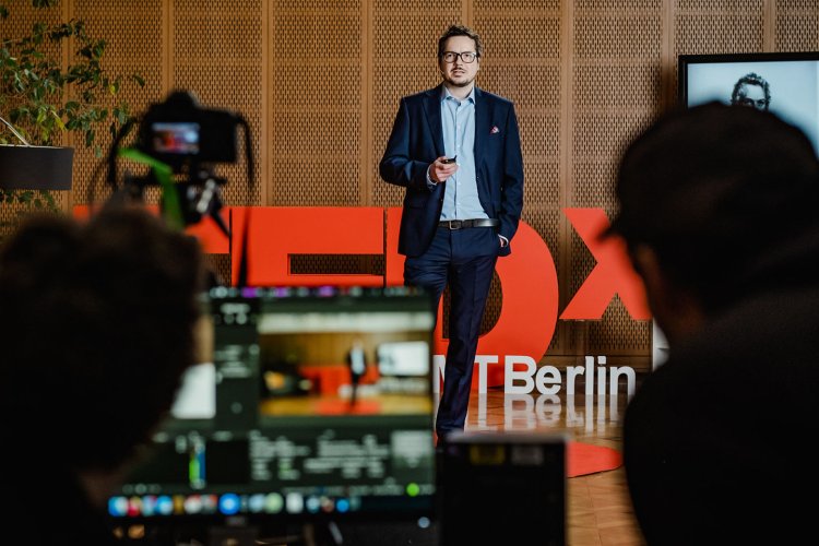 Stefan Wagner speaking at TEDx event at ESMT with blurred view of camera and camera man in front of the stage 