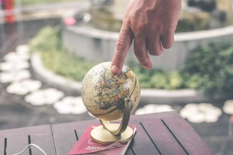 A person's hand touching a small globe atop a passport