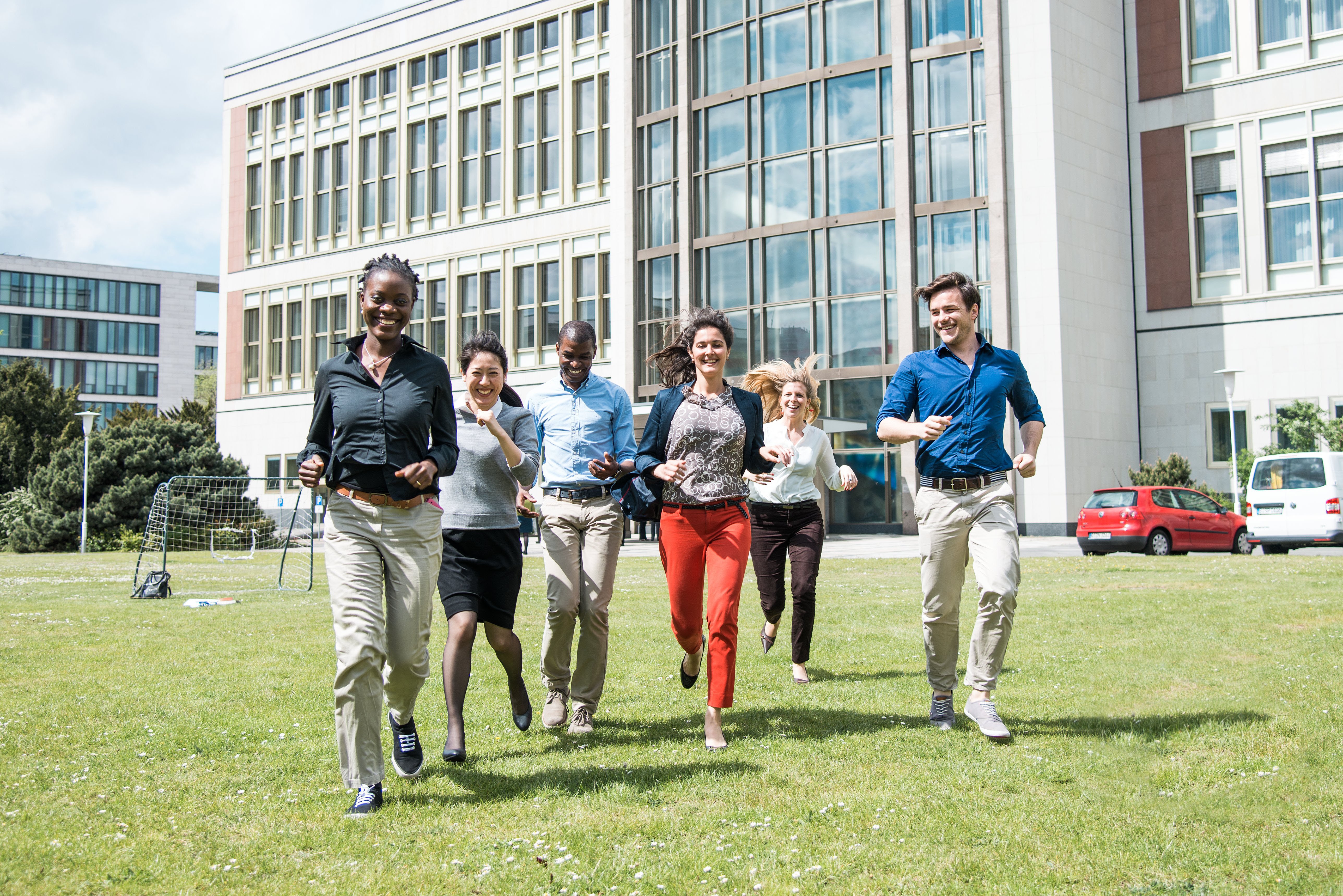 Six students running towards the camra on a green field. 